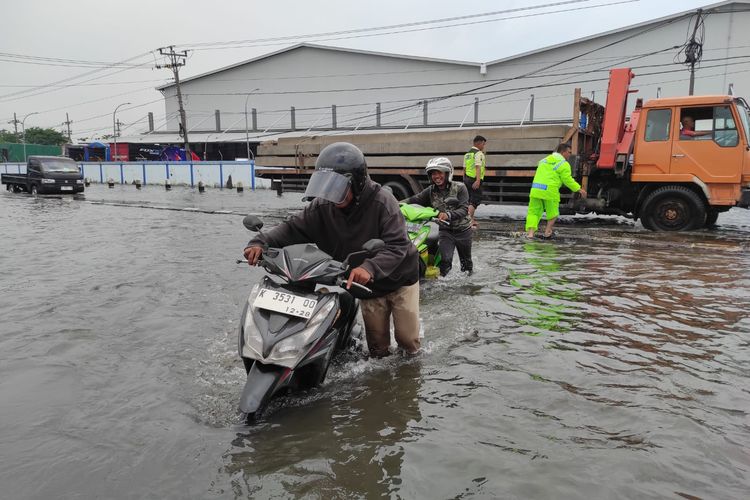 Warga mendorong sepeda motor yang mogok usai nekat menerjang banjir di Pantura Sayung, Kabupaten Demak, Selasa (28/10/2025). 