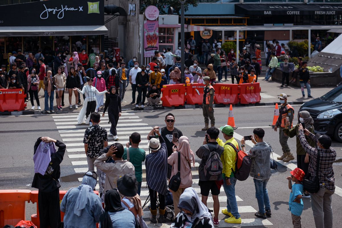 This picture taken on July 24, 2022 shows a crowd looking on as Indonesian youths present self-styled fashion creations at a pedestrian crossing turned catwalk, part of a gathering in recent weeks dubbed Citayam Fashion Week, in Jakarta. The crowd of fashionistas turning one of Jakarta's main commuter hubs into a makeshift catwalk have courted controversy in Indonesia's traffic-clogged capital, but their festival of style has become a site for free expression. (Photo by BAY ISMOYO / AFP) 