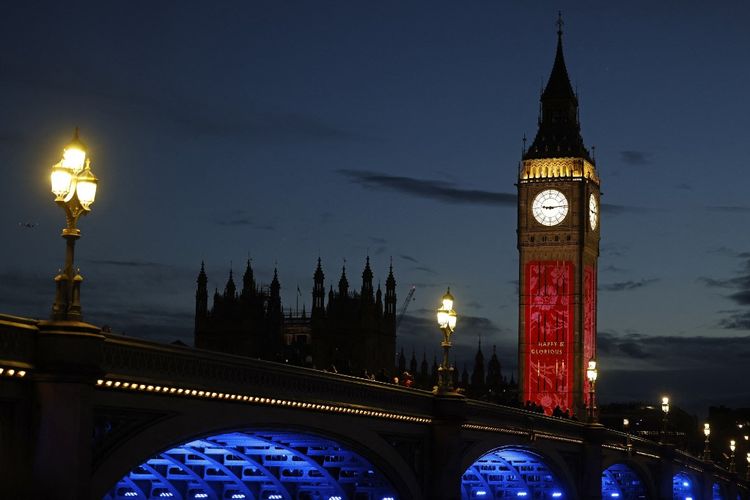 Orang-orang berjalan di Westminster Bridge saat The Elizabeth Tower, atau lebih dikenal sebagai Big Ben, menampilkan proyeksi berbagai gambar di London, Kamis (4/5/2023) menjelang penobatan Raja Charles III.