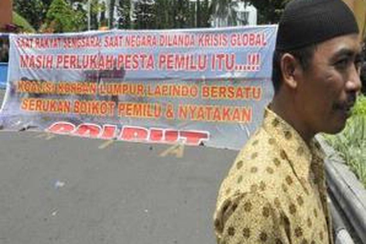 Seorang korban lumpur Lapindo berdiri di depan spanduk ajakan boikot pemilu pada saat unjuk rasa ratusan korban lumpur Lapindo ke Kantor Gubernur Jatim di Surabaya, Senin (30/3).
