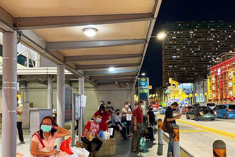 Warga Singapura yang bermasker sedang menunggu bus di halte bus di kawasan Chinatown yang ramai dihiasi lampion Imlek, Rabu malam (26/1/2022).