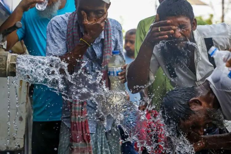 Seorang pria membasuh air ke kepala, sementara orang-orang meminum air dari sebuah kapal tanker selama gelombang panas di Dhaka, Bangladesh, pada 22 April 2024.