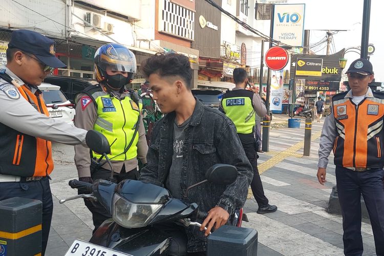 Seorang pengendara motor yang dicegat polisi karena melanggar aturan berlalu lintas di Jalan Margonda Raya, Selasa (16/7/2024).