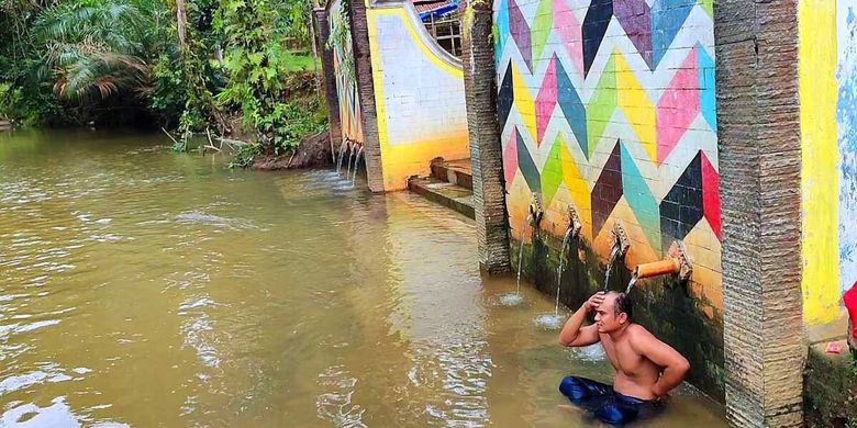 Seorang warga berendam di sungai sambil menikmati pancuran air panas di lokasi wisata Air Panas di Kabupaten Rokan Hulu, Riau, Senin (12/12/2022).