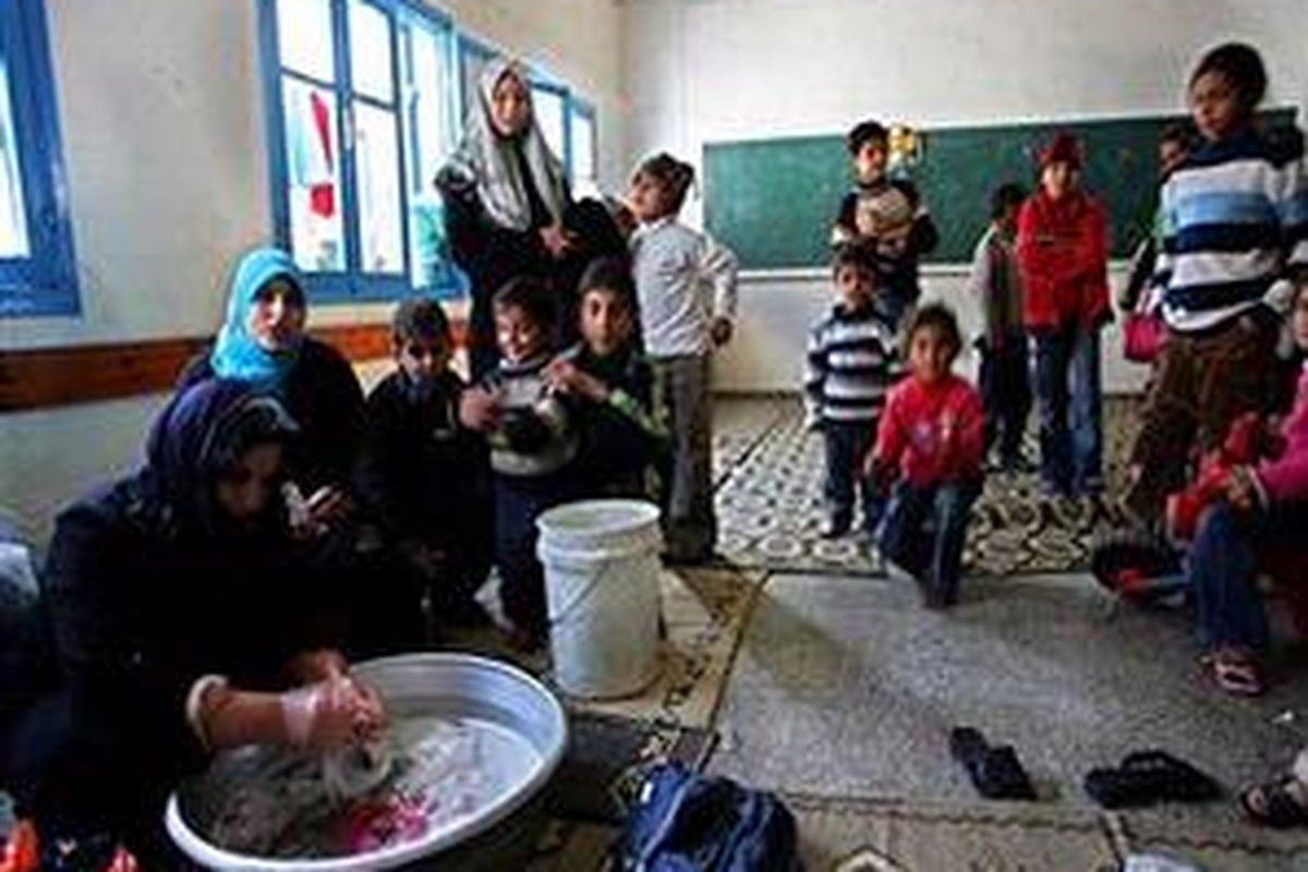 Seorang wanita Palestina mencuci pakaian disaksikan warga lain yang berlindung di Pusat Bantuan  PBB di Rafah, 5 Januari 2009.