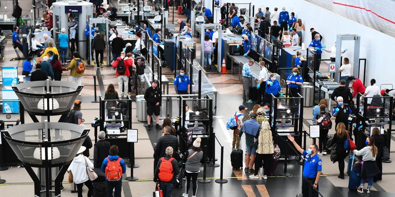 Airline passengers, some not wearing face masks following the end of Covid-19 public transportation rules, wait at a Transportation Security Administration (TSA) checkpoint to clear security before boarding to flights in the airport terminal in Denver, Colorado on April 19, 2022. Mask mandates on public transportation are no longer in effect following a ruling by federal judge on April 18, 2022.