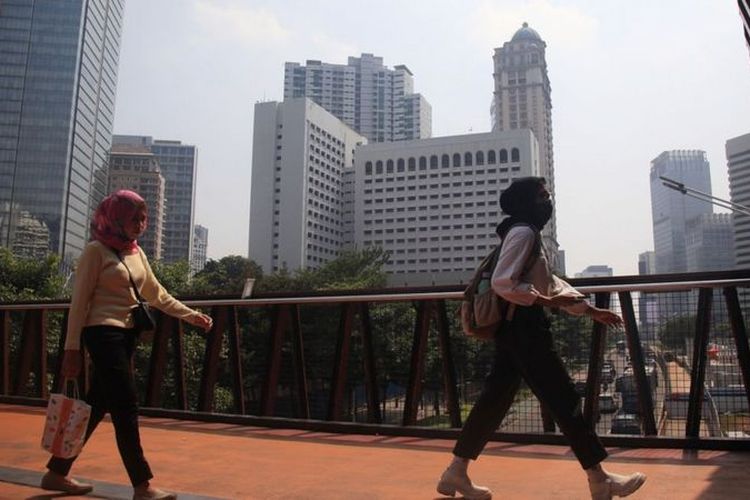 Warga melintas memakai masker untuk melindungi diri dari debu, di Jembatan Penyeberangan Sepeda (JPS) sekaligus Jembatan Penyeberangan Orang (JPO) di Jalan Sudirman,Jakarta, Selasa (8/8/2023)