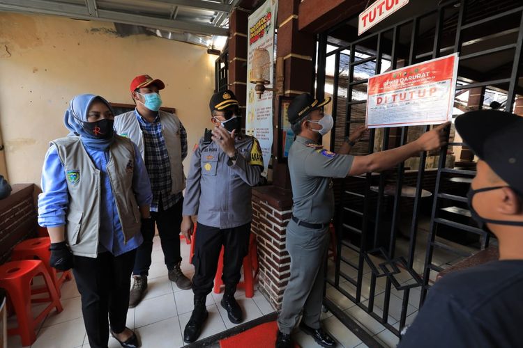 TUTUP—Kasat Pol PP Kota Madiun, Sunardi memasang label penutupan sebuah warung makan yang nekat membuka layanan makan ditempat  disaksikan Wakil Walikota Madiun, Inda Raya Ayu Miko Saputri, Selasa (6/7/2021).