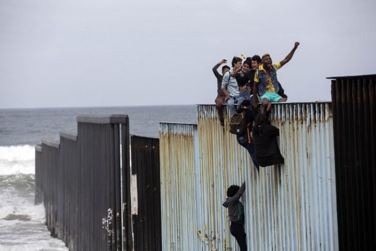 Aksi imigran memanjat pagar perbatasan antara AS-Meksiko di pantai Tijuana, dekat Samudra Pasifik, Minggu (29/4/2018). (AFP/Guillermo Arias)