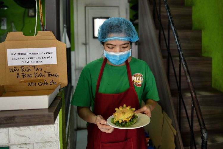 Seorang pelayan mengenakan masker saat menyajikan roti burger bertema Virus Corona di Restoran Pizza Home, di Hanoi, Vietnam, 26 Maret 2020.