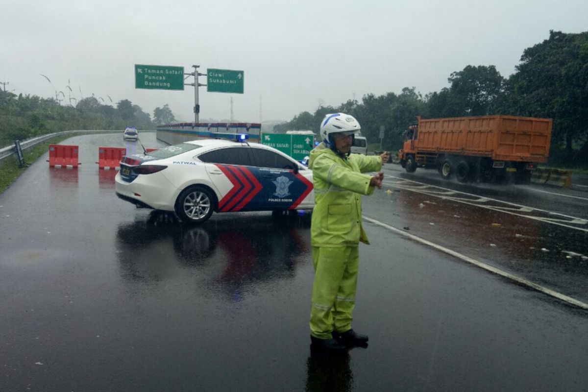 Seorang petugas kepolisian sedang mengalihkan arus kendaraan dari arah Jakarta menuju Puncak, Senin (5/2/2018). Pengalihan arus dilakukan setelah terjadi bencana longsor di sejumlah titik di Jalur Puncak yang menutup badan jalan.