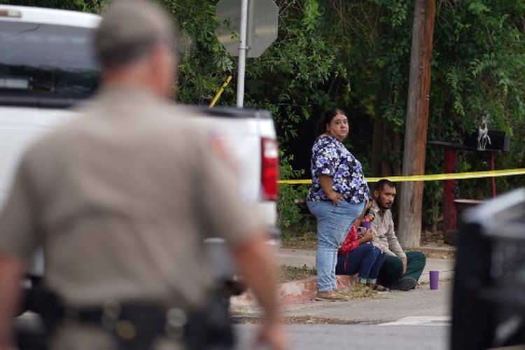 Orang-orang duduk di tepi jalan di luar Robb Elementary School di Uvalde, Texas, pada 24 Mei 2022. Seorang pria bersenjata berusia 18 tahun membunuh 14 anak dan seorang guru di sebuah sekolah dasar di Texas pada hari Selasa, menurut gubernur negara bagian , dalam penembakan sekolah paling mematikan di negara itu selama bertahun-tahun.
