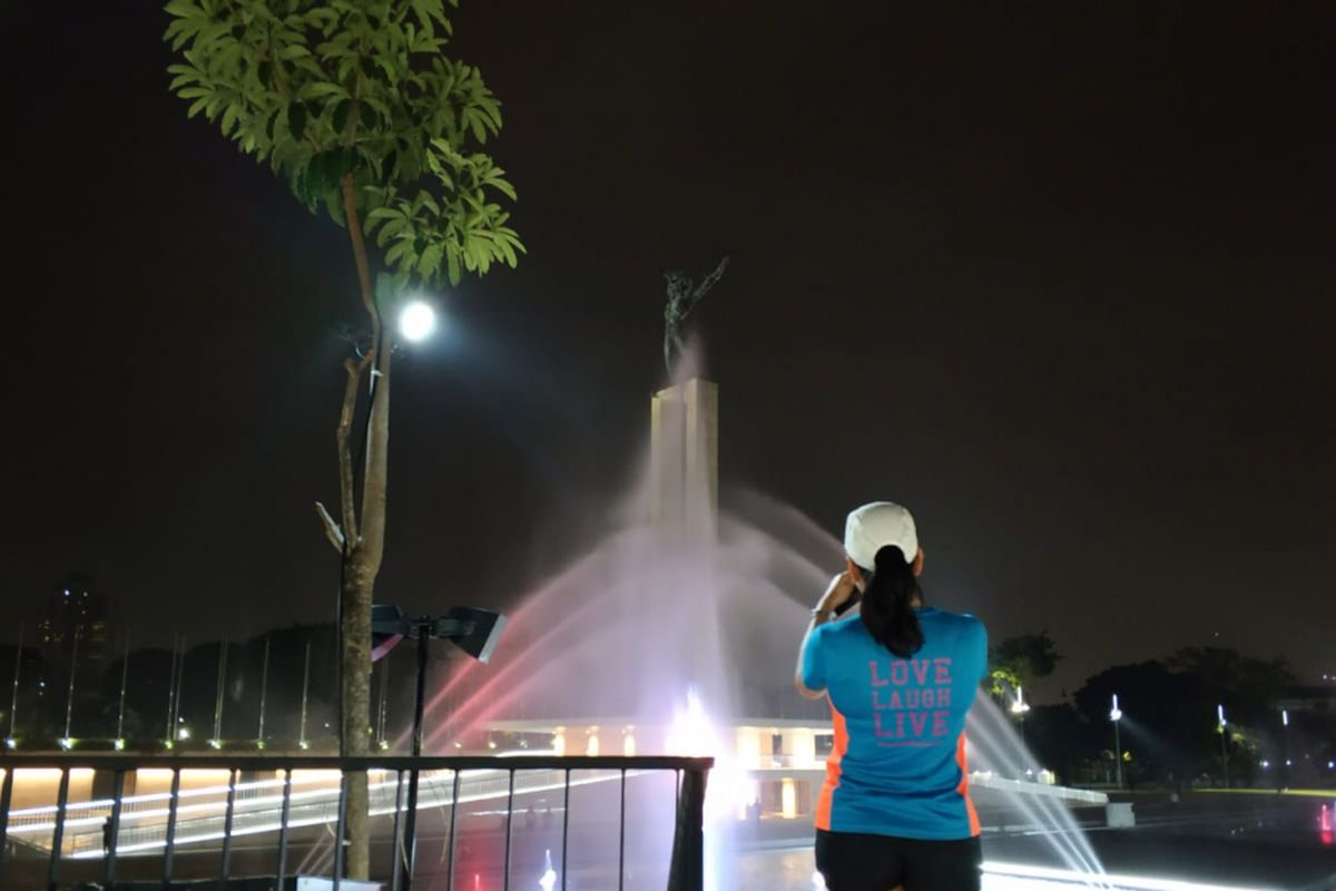 Seorang pengunjung menyaksikan lampu taman yang sedang menyala dan air mancur di Lapangan Banteng, Jakarta Pusat, Rabu (11/7/2018)