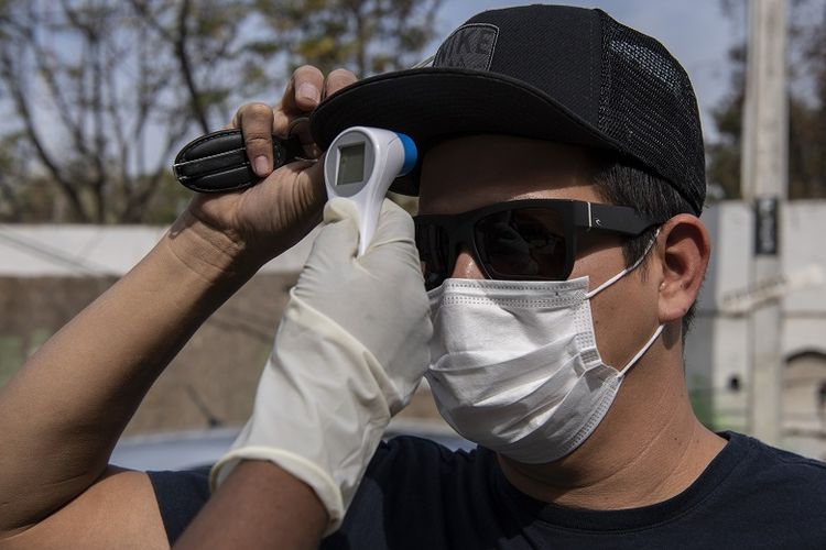 Seorang penjaga keamanan mengukur suhu seorang pria yang mengenakan masker di komune Del Bosque, yang memasuki karantina besok untuk membantu memperlambat penyebaran virus corona alias COVID-19, di Santiago, pada 15 April 2020. - Pihak berwenang Chili telah menerapkan , di antara langkah-langkah lain, karantina selektif di daerah dengan insiden infeksi yang tinggi dan telah menempatkan penekanan pada pengendalian pandemi dengan skrining (penyaringan) massal.