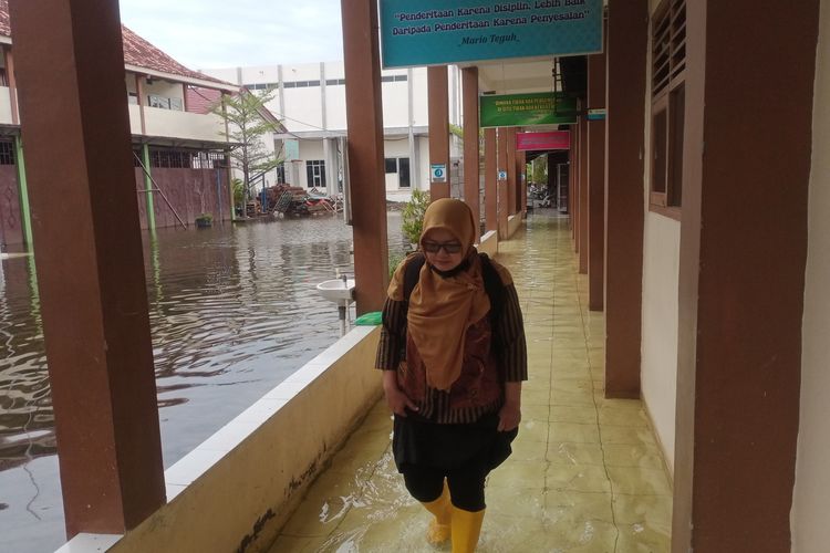 Salah satu guru SMKN 1 Sayung Kabupaten Demak Jawa Tengah saat melintasi genangan rob yang melanda sekolahnya, Rabu (25/5/2022).