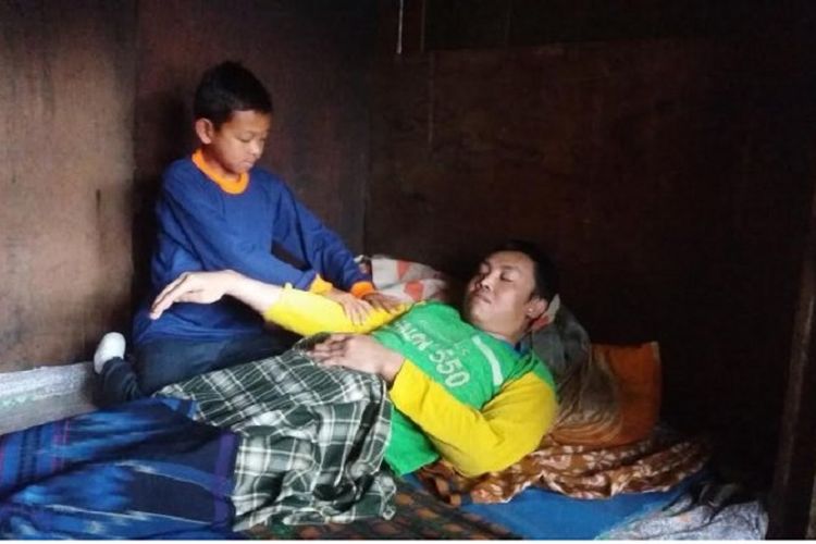 Agus Makmun sedang memijat dan menggantikan pakaian ayahnya, Mahyono yang menderita lumpuh di Dusun Boralan, Garung Wonosobo 