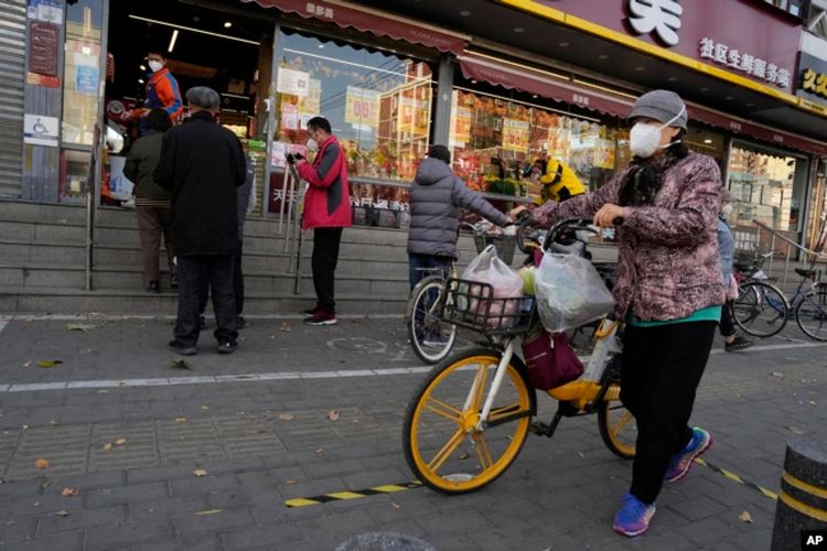 Warga mengenakan masker saat mendorong sepeda dengan barang belanjaannya melewati sebuah toko yang mengontrol arus pembelinya di Beijing, China, Jumat, 25 November 2022.