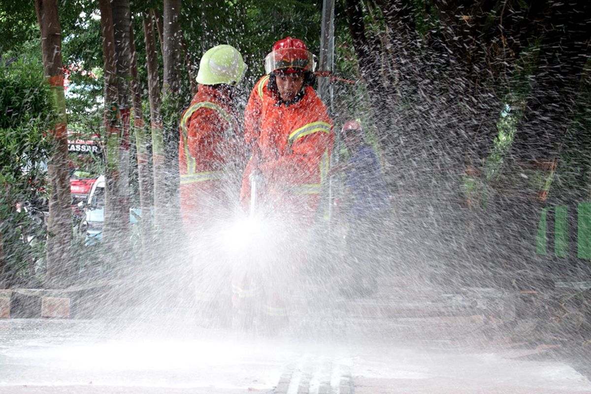 Petugas pemadam kebakaran menyemprotkan cairan disinfektan ke trotoar di Makassar, Sulawesi Selatan, Minggu (22/3/2020). Penyemprotan cairan disinfektan tersebut  guna mengurangi resiko penularan virus corona atau COVID-19 di sejumlah are publik mengingat telah ditemukannya dua kasus positif di Sulsel dan salah satu diantaranya meninggal dunia.