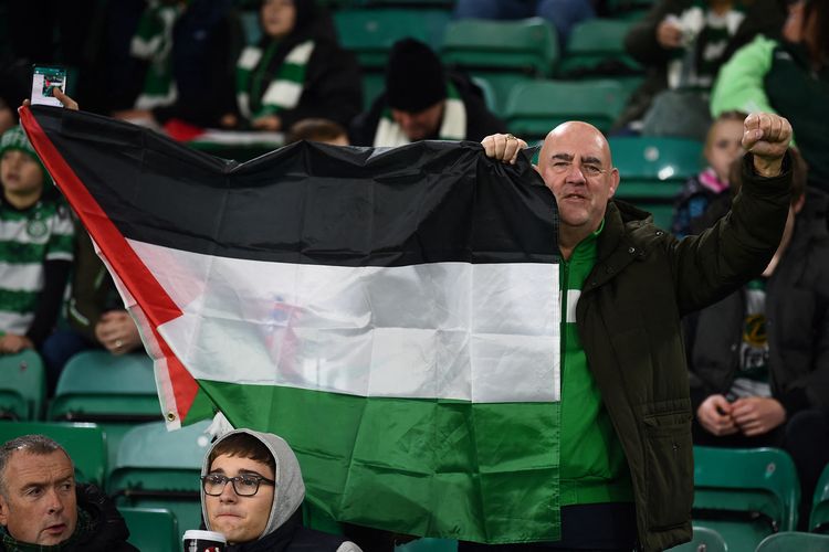 Seorang suporter memegang bendera Palestina sebelum dimulainya pertandingan sepak bola grup E Liga Champions UEFA antara Celtic dan Atletico Madrid di stadion Celtic Park, Glasgow, Skotlandia, 25 October 2023. (Photo by ANDY BUCHANAN / AFP)