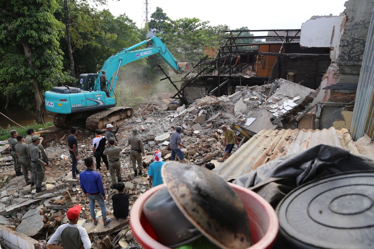 Petugas Satpol PP melalui dua back hoe membongkar bangunan semi permanen yang berada di area bantaran aliran Sungai Ciliwung di RW 01 Bukit Duri, Jakarta Selatan, Selasa (11/7/2017). Setelah bangunan diratakan dengan tanah, Balai Besar Sungai Ciliwung Cisadane (BBWSCC) akan memulai memasang sheet pile sebagai lanjutan proyek normalisasi Ciliwung.