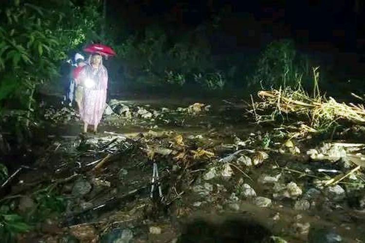 Seorang wanita yang menggendong anak membawa lampu penerang melintasi jalan yang tertutup material banjir di jalur jalan pesisir selatan Kabupaten Bone Bolango. Jalan yang menghubungkan Provinsi Gorontalo dan Sulawesi Utara ini masih belum dilalui kendaraan.