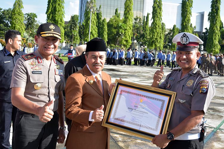 Gubernur Riau Syamsuar (tengah) menyerahkan penghargaan kepada petugas polisi Bripka Ralon Manurung pada peringatan Hari Guru di Kota Pekanbaru, Riau, Senin (25/11/2019). Bripka Ralon Manurung menerima dua penghargaan dari Gubernur Riau dan Kapolda Riau pada peringatan Hari Guru, karena dinilai berjasa membantu pembangunan sekolah marjinal dari uang pribadinya di pelosok Kabupaten Kampar.