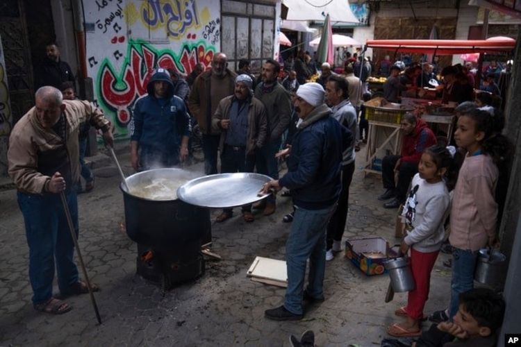 Warga Palestina, Walid Hattab tengah memasak makanan berbuka puasa berupa sup dan bubur gandum untuk penduduk yang kurang mampu 