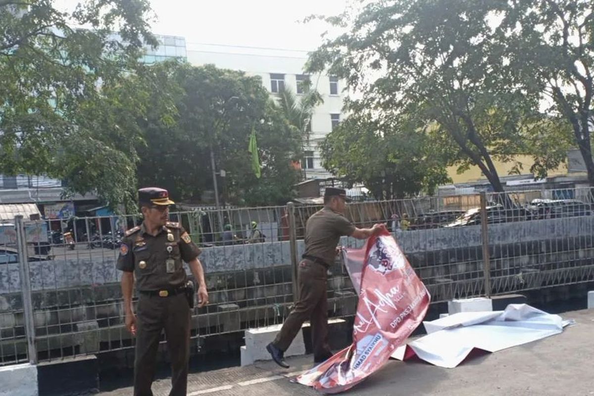 Petugas Satpol PP DKI Jakarta mencopot spanduk politik di pinggir jalan.