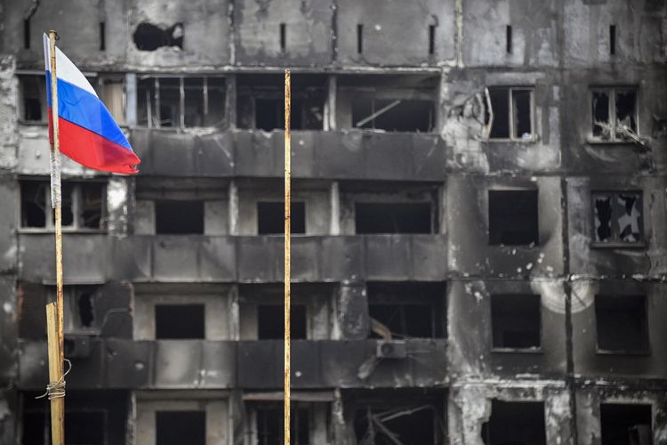 Bendera Rusia berkibar di depan bangunan yang hancur di Mariupol, Ukraina, 12 April 2022. Perang Ukraina-Rusia terkini memperebutkan kota pelabuhan Mariupol di Ukraina timur.