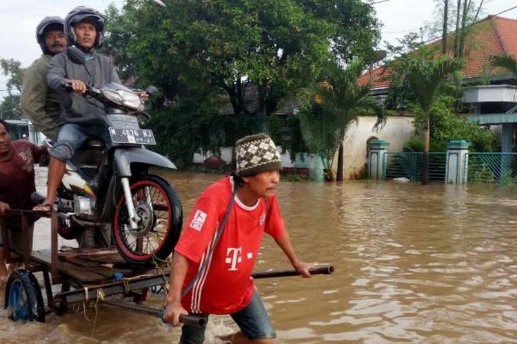 Seorang jasa angkut sedang menarik pengendara motor dengan gerobak sebelum genangan air surut yang sempat menutup jalur pantura Pasuruan-Probolinggo, Selasa pagi (31/1/2017).