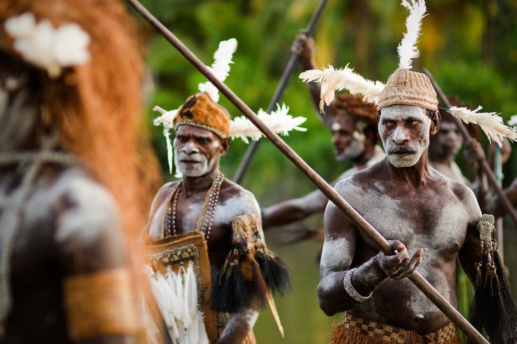 Penduduk dari Suku Asmat, Papua yang menggunakan pakaian adat dan membawa senjata tradisional berupa tombak.