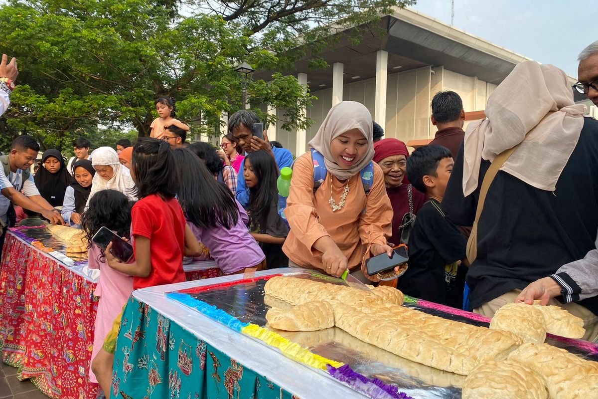 Pengunjung Taman Indonesia Indah (TMII) mengambil potongan roti buaya untuk dinikmati bersama di Plaza Kori Agung, TMII, Jakarta Timur, Sabtu (22/6/2024).