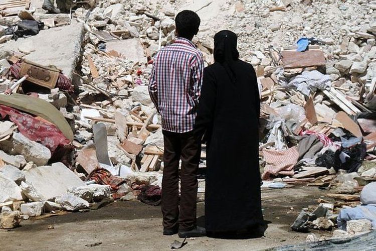 Pasangan suami-istri menyaksikan upaya evakuasi tim penolong di tengah reruntuhan akibat serangan bom di sudut Kota Aleppo, Suriah, 28 April 2014.