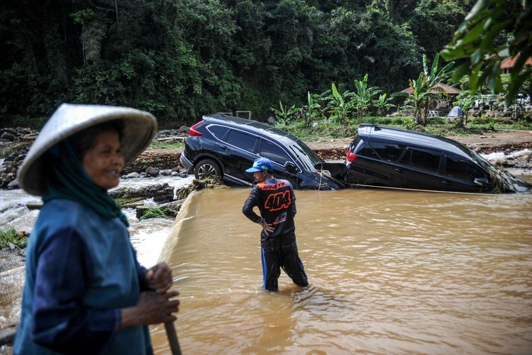 Warga menyaksikan proses evakuasi dua buah mobil yang terseret arus banjir bandang di Citengah, Sumedang Selatan, Kabupaten Sumedang, Jawa Barat, Kamis (5/5/2022). Banjir bandang yang disebabkan luapan Sungai Cihonje akibat hujan deras pada Rabu (4/5/2022) sore tersebut membuat puluhan rumah terdampak, dua kendaraan hanyut dan satu orang korban masih dalam pencarian.