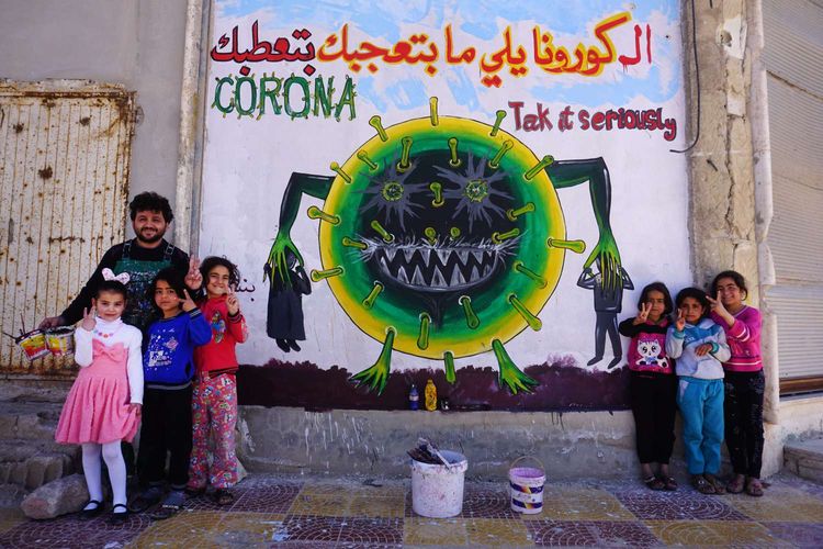 Seniman mural asal Suriah Aziz al-Azmar bersama anak-anak berpose di depan mural bertemakan virus corona yang baru saja selesai di Binnish, Suriah, 23 Maret 2020. Pandemi Covid-19 yang disebabkan oleh virus corona menjadi insipirasi seniman grafiti untuk memberikan peringatan dan motivasi bagi warga dalam menghadapi virus tersebut.