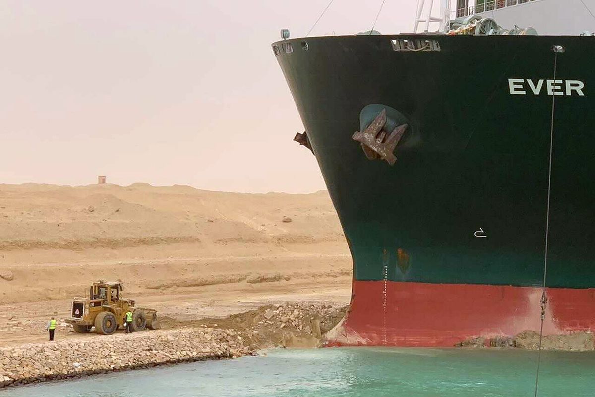 Foto yang dirilis Otoritas Terusan Suez menunjukkan kapal kargo Ever Given yang haluannya tersangkut di dinding kanal pada Rabu (24/3/2021). Insiden ini membuat Terusan Suez macet, dan 150 kapal mengantre untuk melintas. Harga minyak dunia pun naik karena keterlambatan pengiriman.
