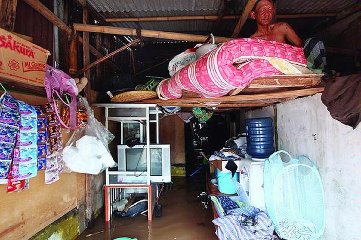 Seorang warga bernama Nasir duduk di papan darurat di rumahnya yang tergenang banjir di kawasan Kedoya Selatan, Jakarta Barat,  Minggu (25/11). Walaupun sempat surut, banjir di sejumlah lokasi di Jakarta kembali naik seiring meluapnya sungai-sungai di Jakarta.
