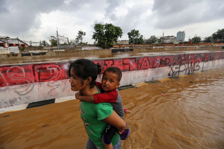 Warga berjalan melintasi banjir di Kampung Pulo, Jatinegara, Jakarta Timur, Selasa (6/2/2018). Banjir merendam ratusan rumah warga akibat luapan air dari Sungai Ciliwung.