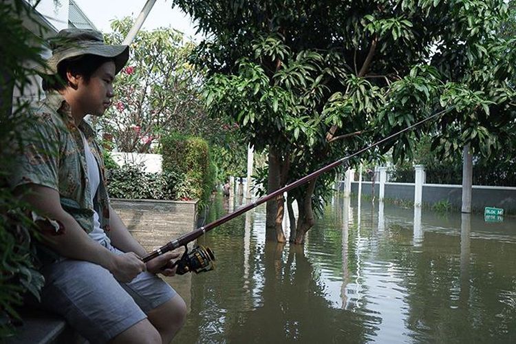 Putra Basuki Tjahaja Purnama, Nicholas Sean Purnama, bergaya memancing di depan rumahnya yang diterjang banjir rob.
