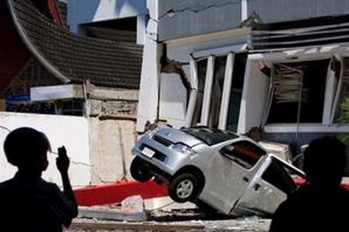 Warga menyaksikan sebuah mobil yang tertimpa bangunan akibat gempa di Padang, Sumatera Barat, Jumat (2/10). Gempa bumi berskala 7,6 skala richter yang mengguncang Padang mengakibatkan sedikitnya 500 orang meninggal dan ribuan bangunan hancur. 