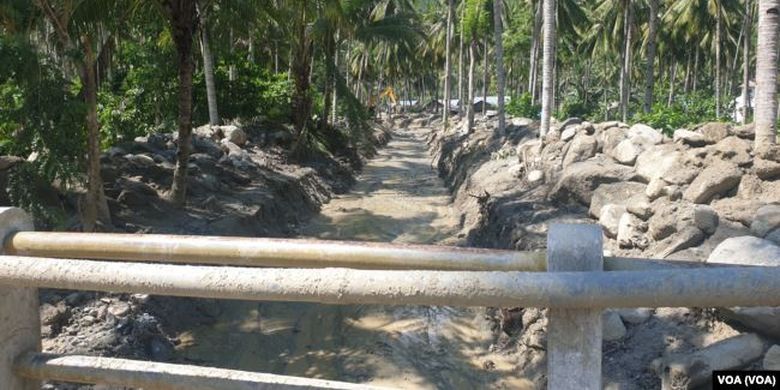 Alat berat ekskavator membersihkan aliran sungai mati di desa Poi yang dipenuhi material pasir bercampur batu-batu besar yang terbawa banjir bandang, 9 Desember 2019. 