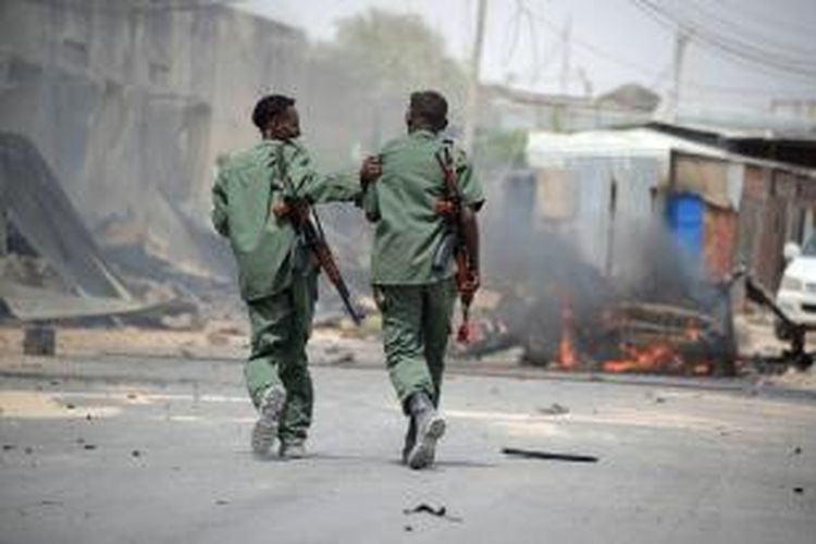 Dua orang prajurit Somalia melintasi lokasi bom mobil bunuh diri yang menghantam konvoi kendaraan PBB di dekat bandara Mogadishu, Kamis (13/2/2014). Insiden itu menewaskan enam orang,