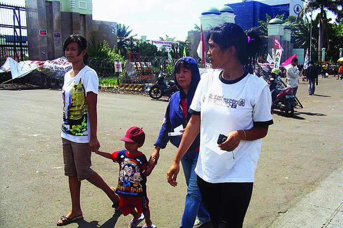 Deasy Arien (tengah) menggandeng cucunya, Gilang Ramadan (2), didampingi dua putrinya, Rani Gantini (kanan) dan Mia Romlah, saat berdemonstrasi di depan Gedung MPR/DPR/DPD, Kamis (28/1). Keluarga itu menyediakan tidak kurang dari 200 nasi bungkus untuk para demon st r a n .