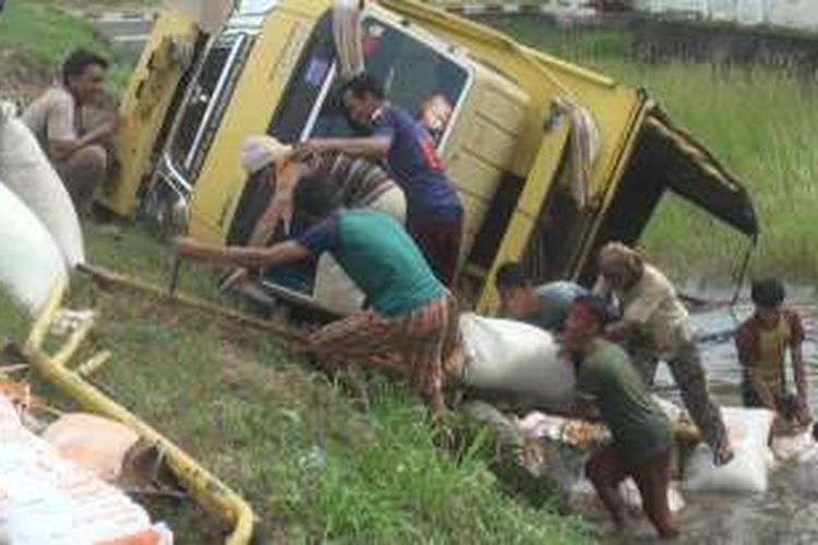 Warga membantu mengeluarkan puluhan karung yang tumpah ke parit berisi air akibat truk pengangkutnya terjungkal