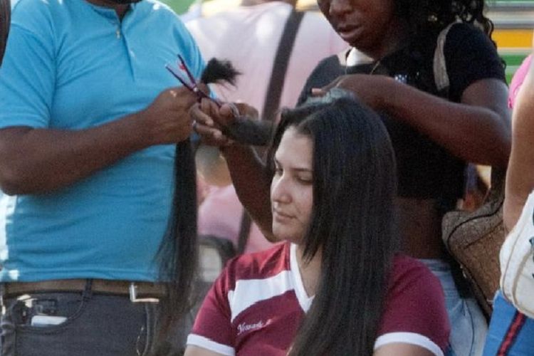 Seorang perempuan Venezuela terlihat memotong rambutnya dalam upaya mendapatkan uang di perbatasan Kolombia. Warga Venezuela ada yang mengungsi sejak inflasi di negara tersebut meningkat.