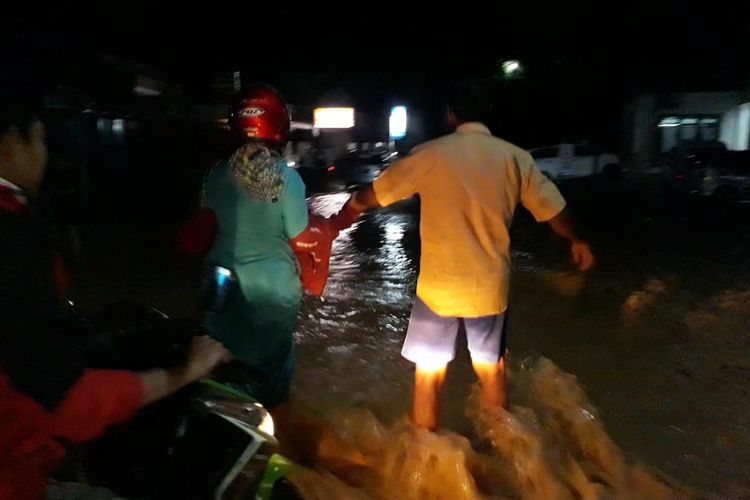 Akibat banjir, pengendara motor terpaksa dievakuasi untuk melintasi jalan yang terendam dengan kondisi arus deras, Sabtu (27/03/2021)