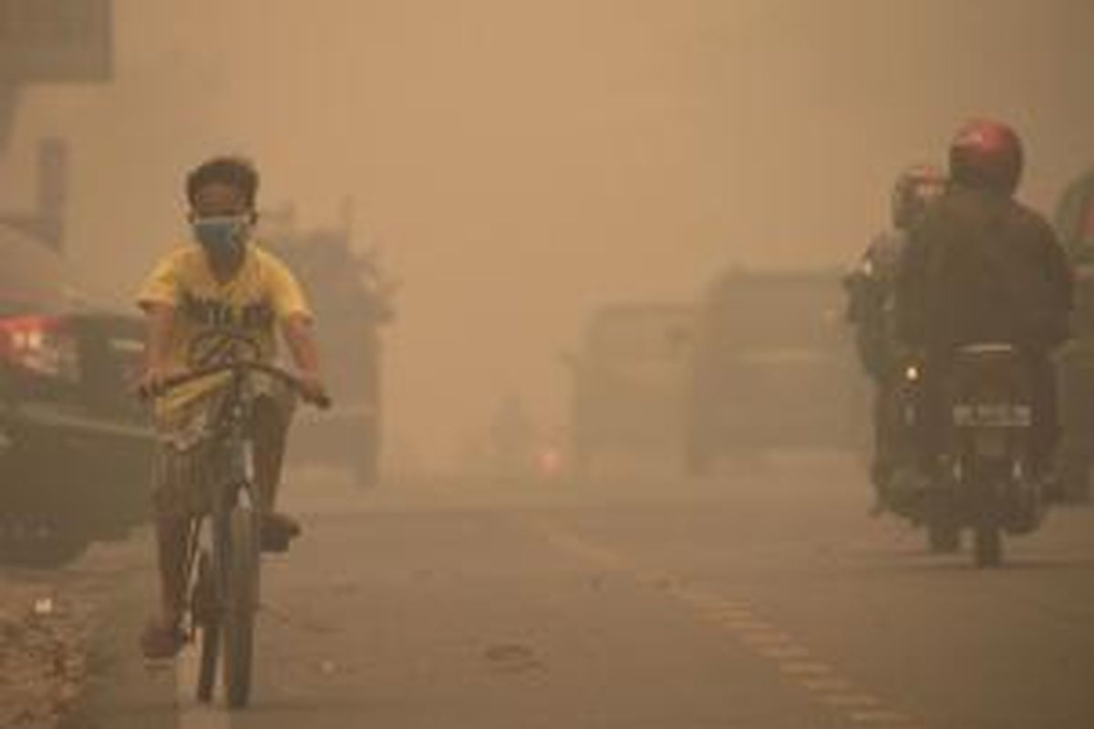 Seorang anak bersepeda dengan menggunakan masker di Kota Pekanbaru, Riau, Kamis (13/3/2014). Kabut asap yang disebabkan kebakaran lahan dan hutan tersebut semakin pekat. Pemerintah Provinsi Riau mengimbau warga untuk menggunakan masker terkait kualitas udara yang memburuk. 