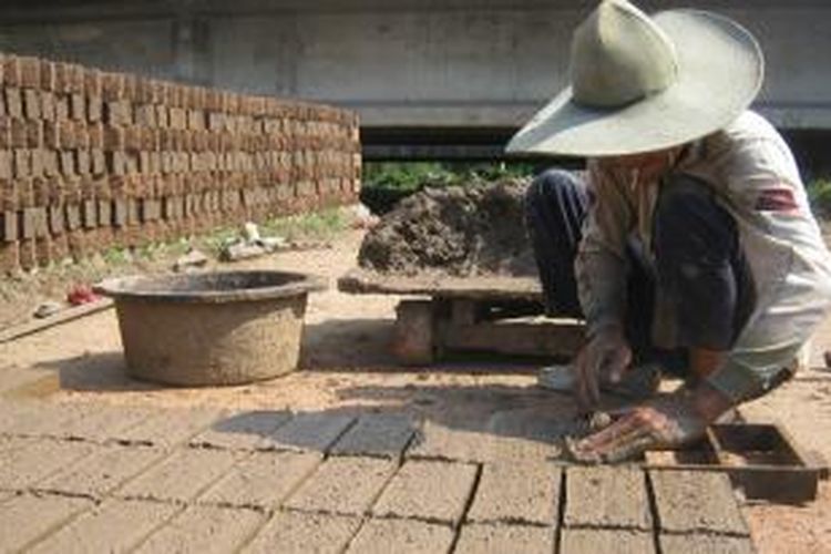 Seorang perajin batu bata sedang mencetak adonan tanah liat yang diambil dari endapan sungai yang dicampur sekam padi.