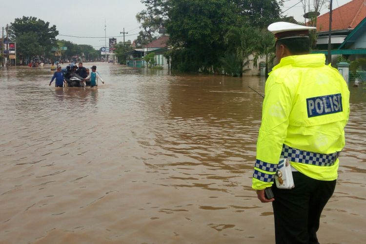 Seorang polisi sedang memantau kondisi jalur pantura di wilayah Kraton Pasuruan yang lumpuh total akibat genangan air setinggi satu meter.