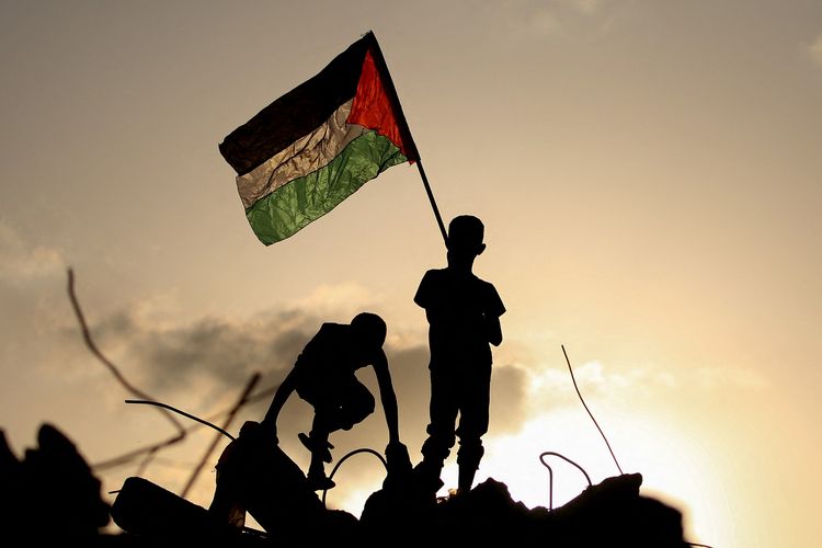 Anak pengungsi mengibarkan bendera Palestina saat berdiri di atas reruntuhan bangunan di kamp pengungsian Bureij, tengah Jalur Gaza, 22 September 2025. Menlu Indonesia Sugiono sebut 10 negara sepakat bentuk tim kecil sebelum 25 September untuk bahas pembentukan negara Palestina pascaperang.